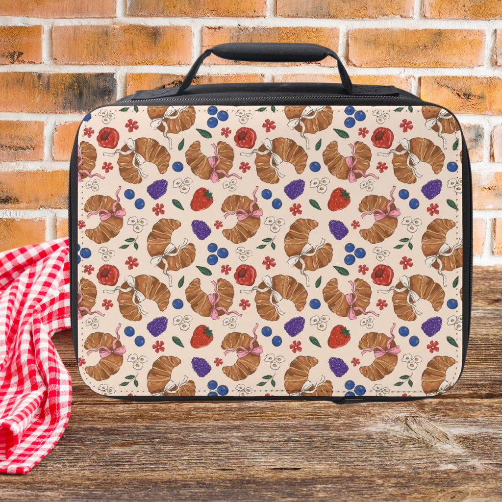 Patterned lunch bag with croissant design on a wooden surface and brick wall background