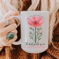 Person holding a 15oz mug with a hand drawn floral design and text on a textured surface