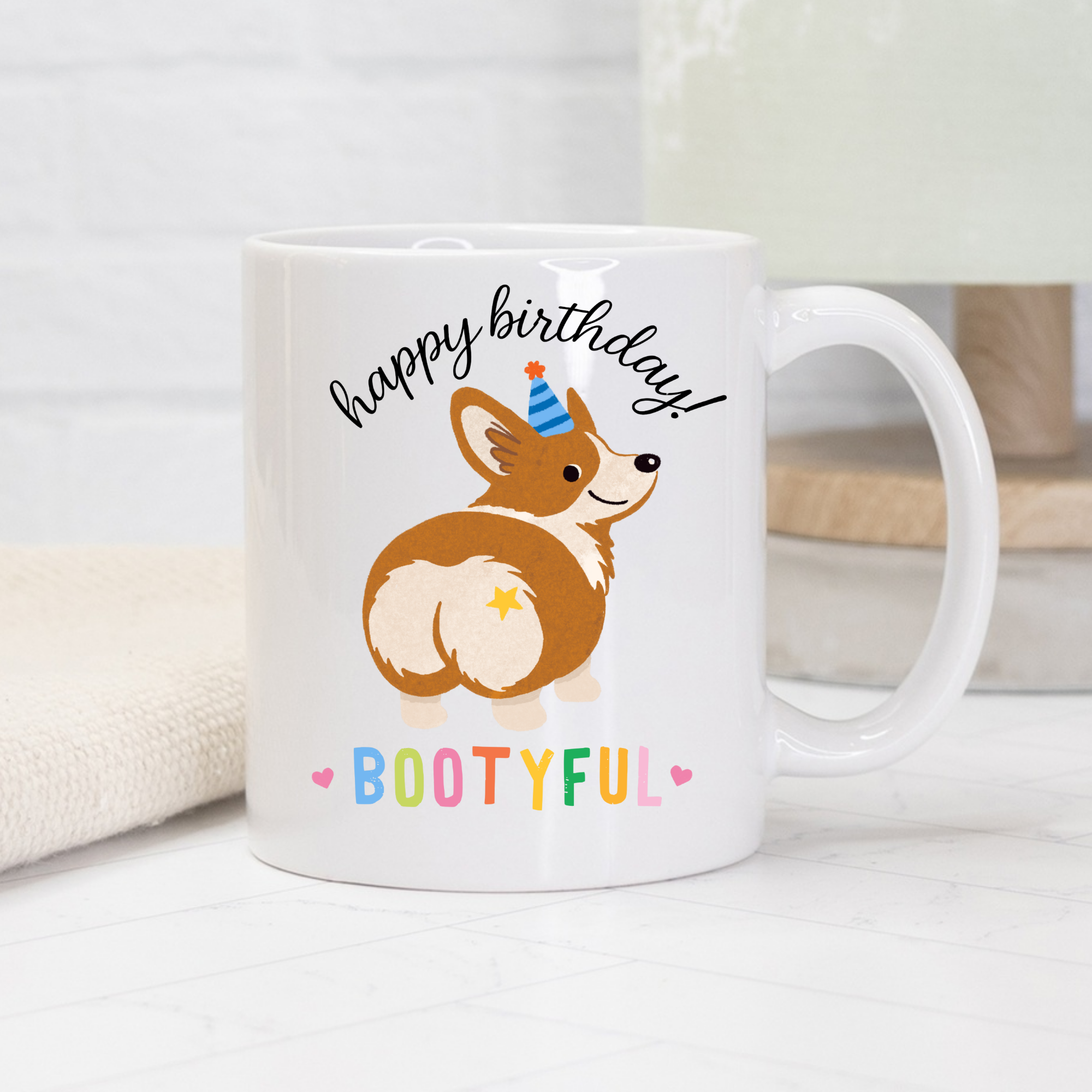 White mug with a corgi illustration and 'happy birthday! Bootyful' text on a white background