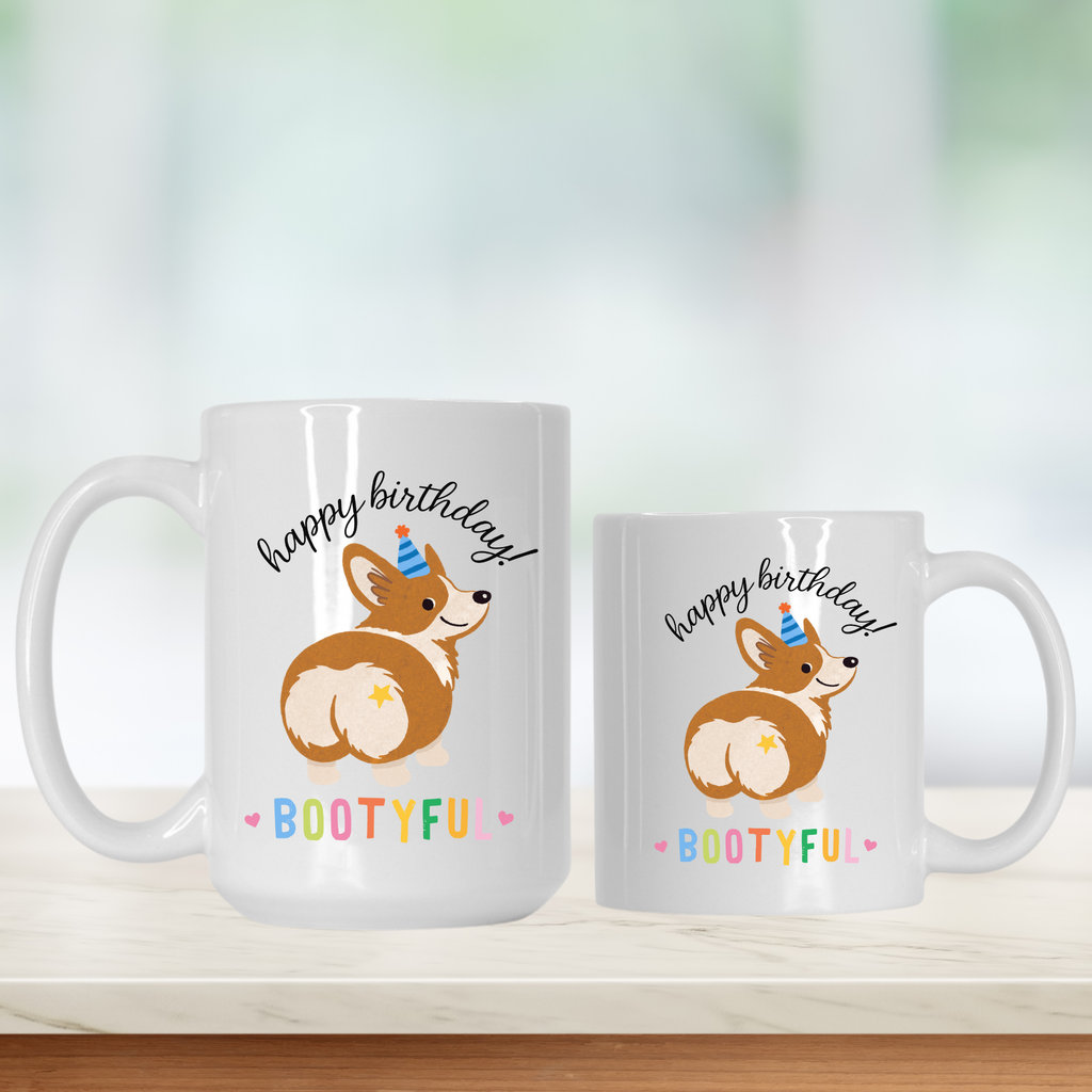 Two white mugs with a corgi design and 'happy birthday bootyful' text on a light background.