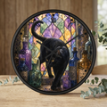 Round wall clock with a black cat walking in front of a stained-glass-style multicolor background, surrounded by illustrated bottles, displayed on a wooden surface with eucalyptus leaves.