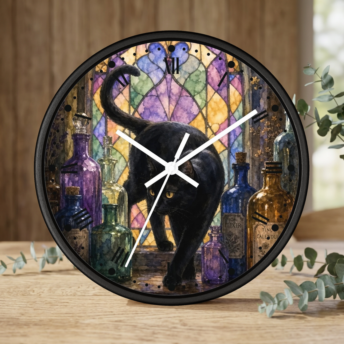 Round wall clock with a black cat walking in front of a stained-glass-style multicolor background and surrounded by colorful glass bottles, shown standing on a wooden surface with eucalyptus leaves around it.