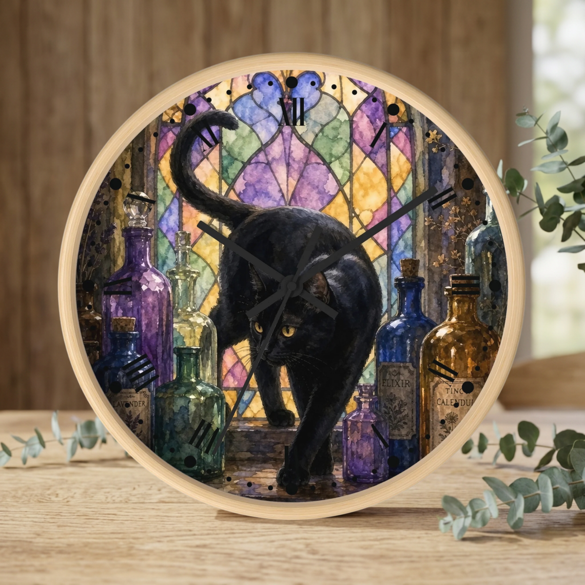 Round wall clock with a light wood frame, featuring a printed illustration of a black cat in front of a colorful stained-glass window with potion bottles. The clock is shown standing on a wooden surface with eucalyptus branches.