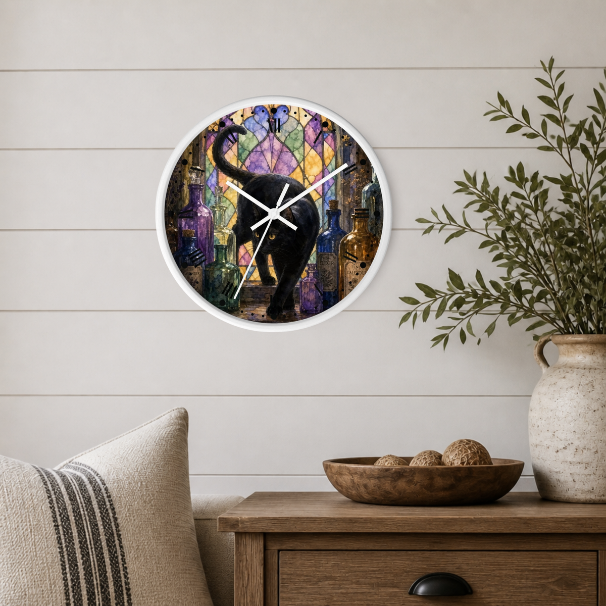 A round wall clock with a white frame hangs on a light wood shiplap wall above a wooden side table. The clock face features a colorful stained-glass-style illustration of a black elephant surrounded by purple, blue, and gold tones.