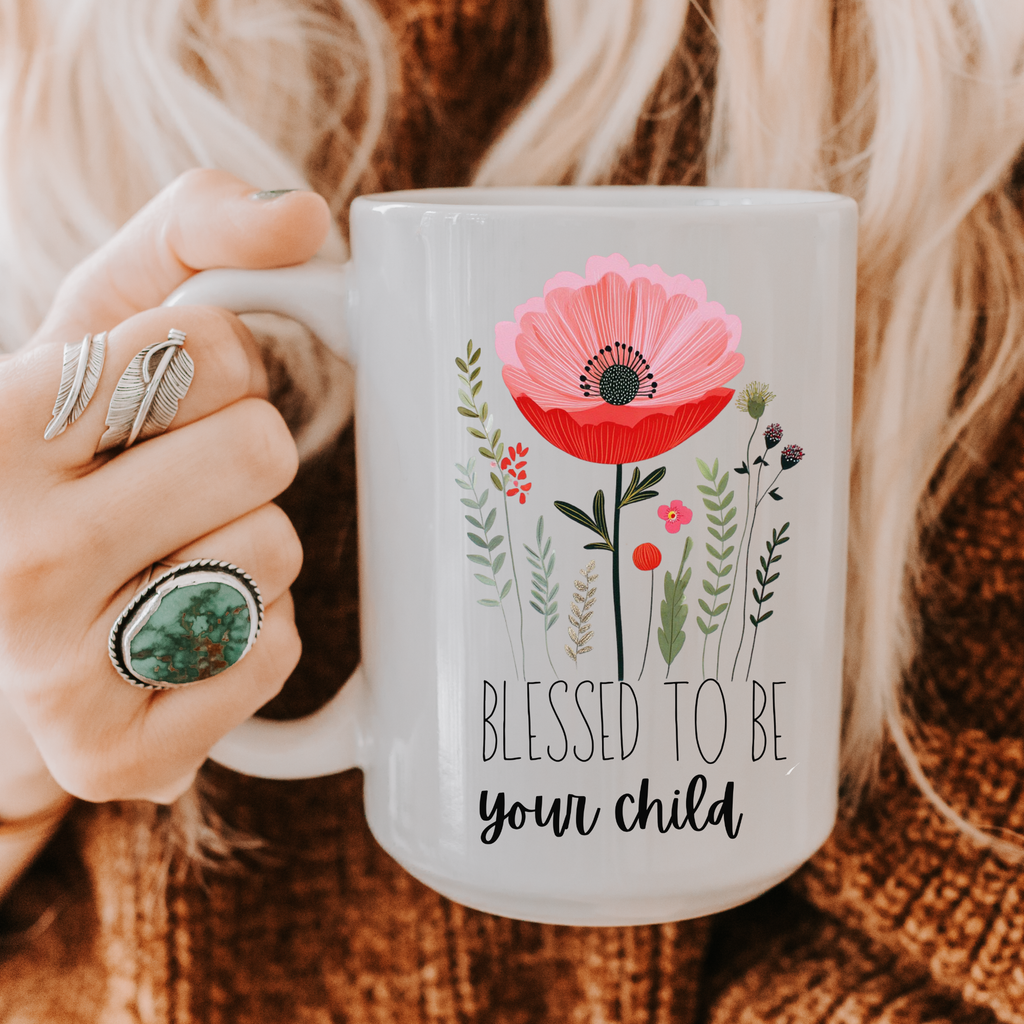 Person holding a 15oz mug with floral design and 'Blessed to be your child' text