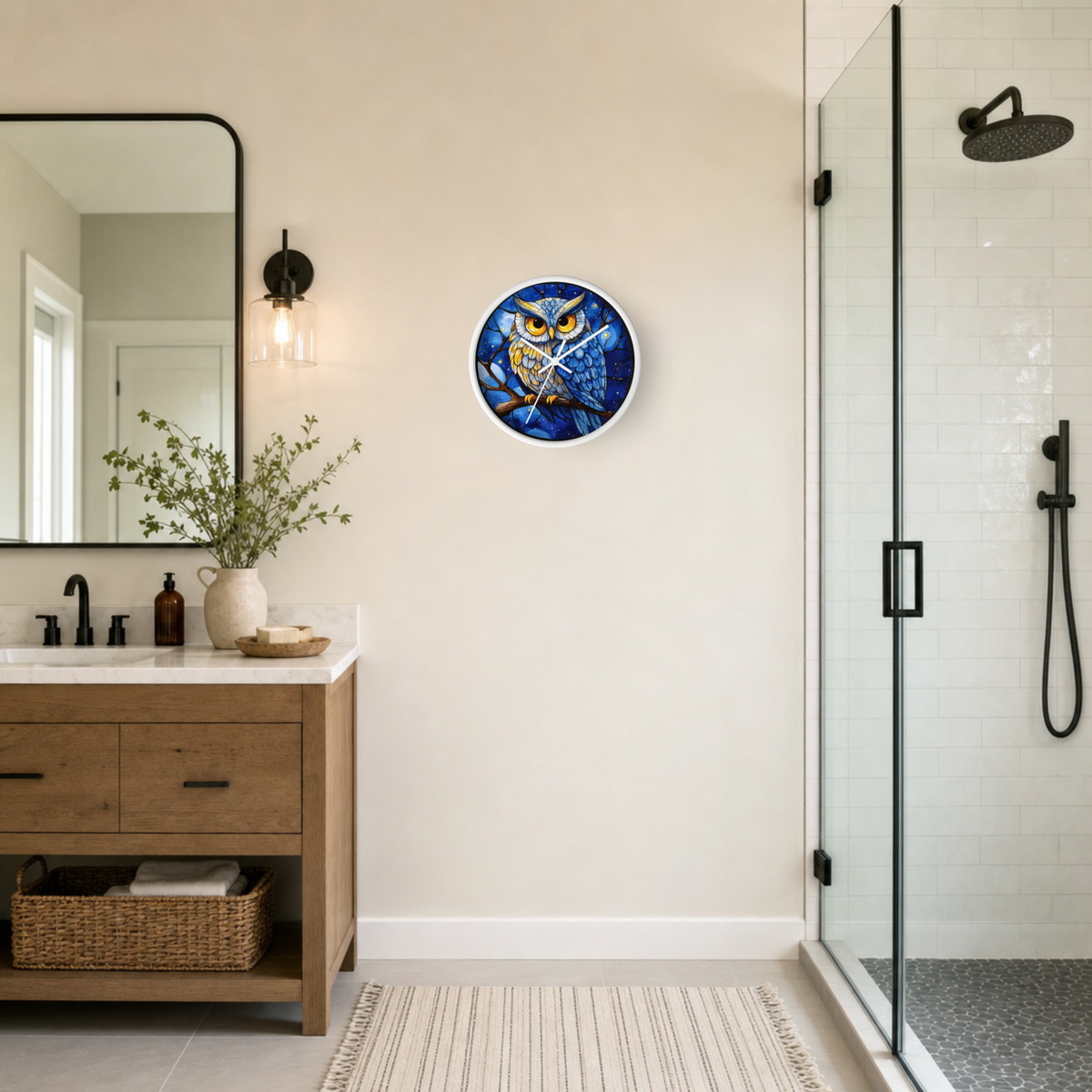 A round wall clock featuring a colorful owl illustration in shades of blue, yellow, and orange, mounted on a beige wall in a modern bathroom setting with a wooden vanity, mirror, and glass shower enclosure.