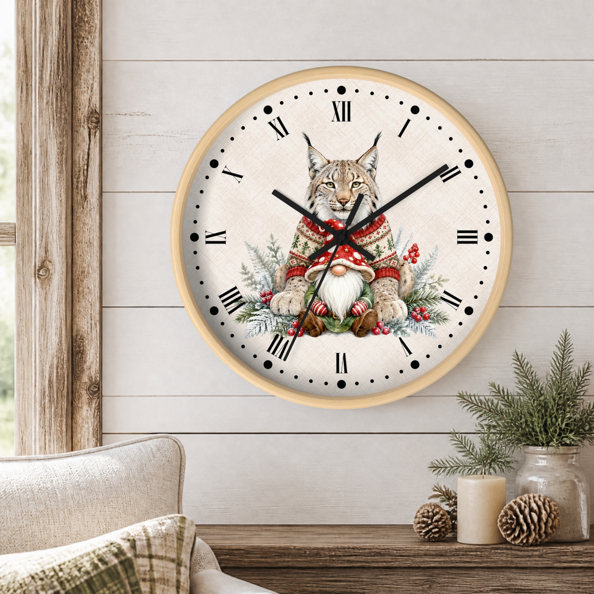 A round wall clock with a light wood frame hangs on a white shiplap wall above a rustic wooden table. The clock face features a detailed illustration of a lynx cat wearing a red knit sweater and a white bearded gnome, surrounded by green pine branches and red berries.