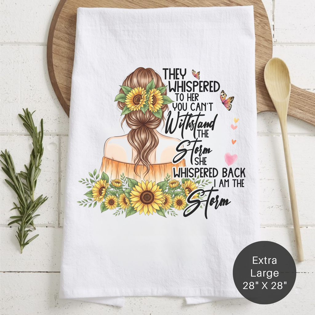 White tea towel with a design of a woman with flowers in her hair and text, placed on a wooden surface with kitchen items.