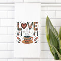 Decorative tea towel with 'LOVE' and coffee cup design on a white tiled wall.