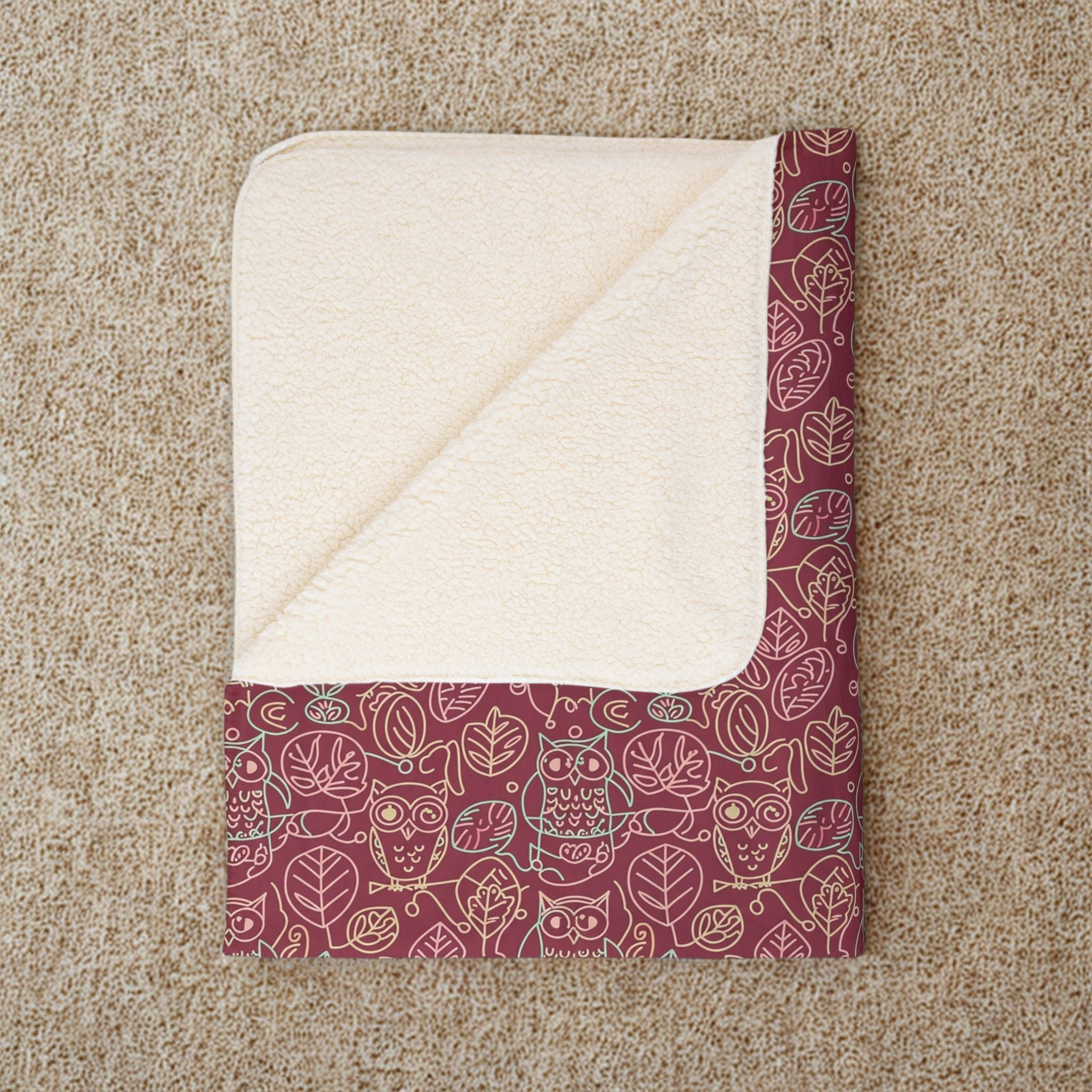 Folded blanket with a red and white owl pattern on a beige carpet