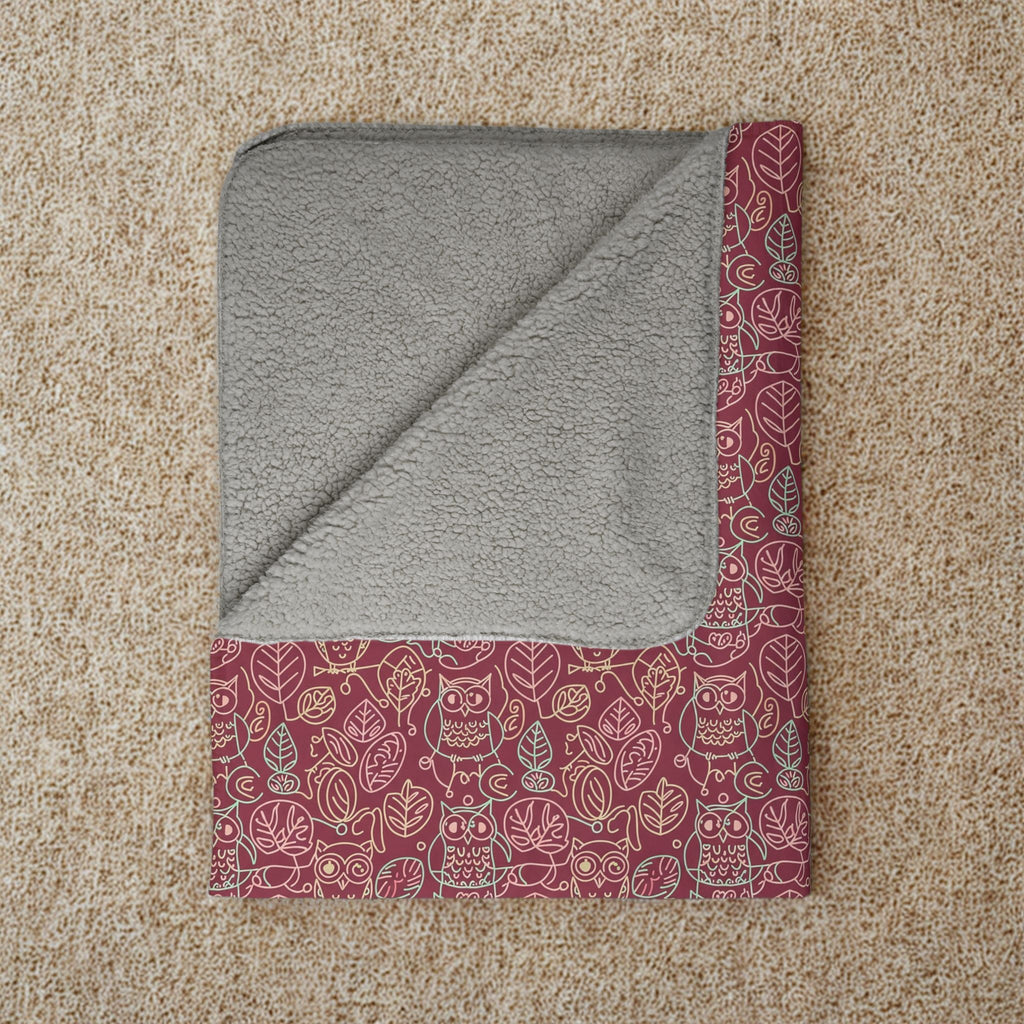 Folded blanket with gray interior and red owl patterned exterior on a beige carpet