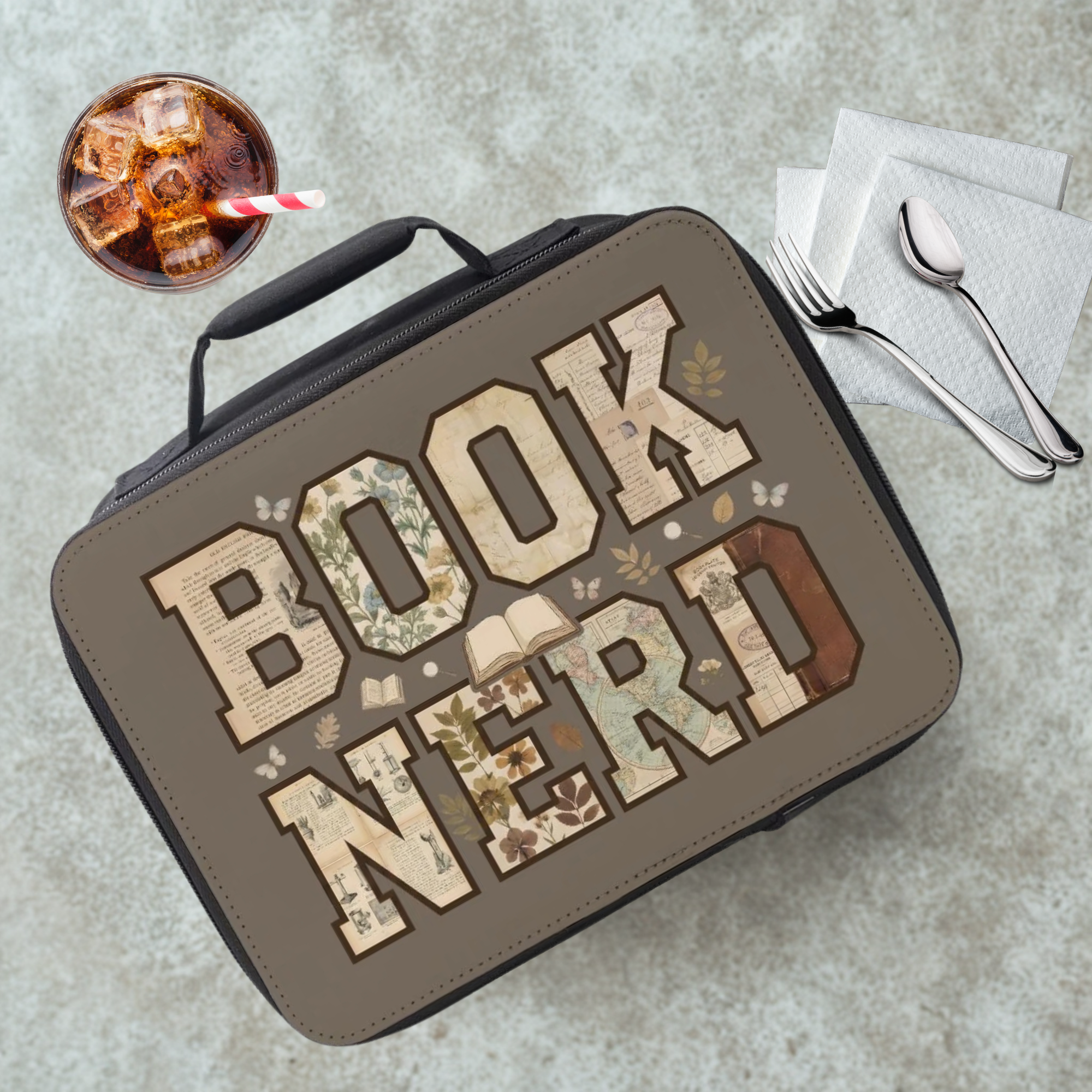 Lunch bag with 'BOOK NERD' text on a cafeteria table with a drink and utensils.