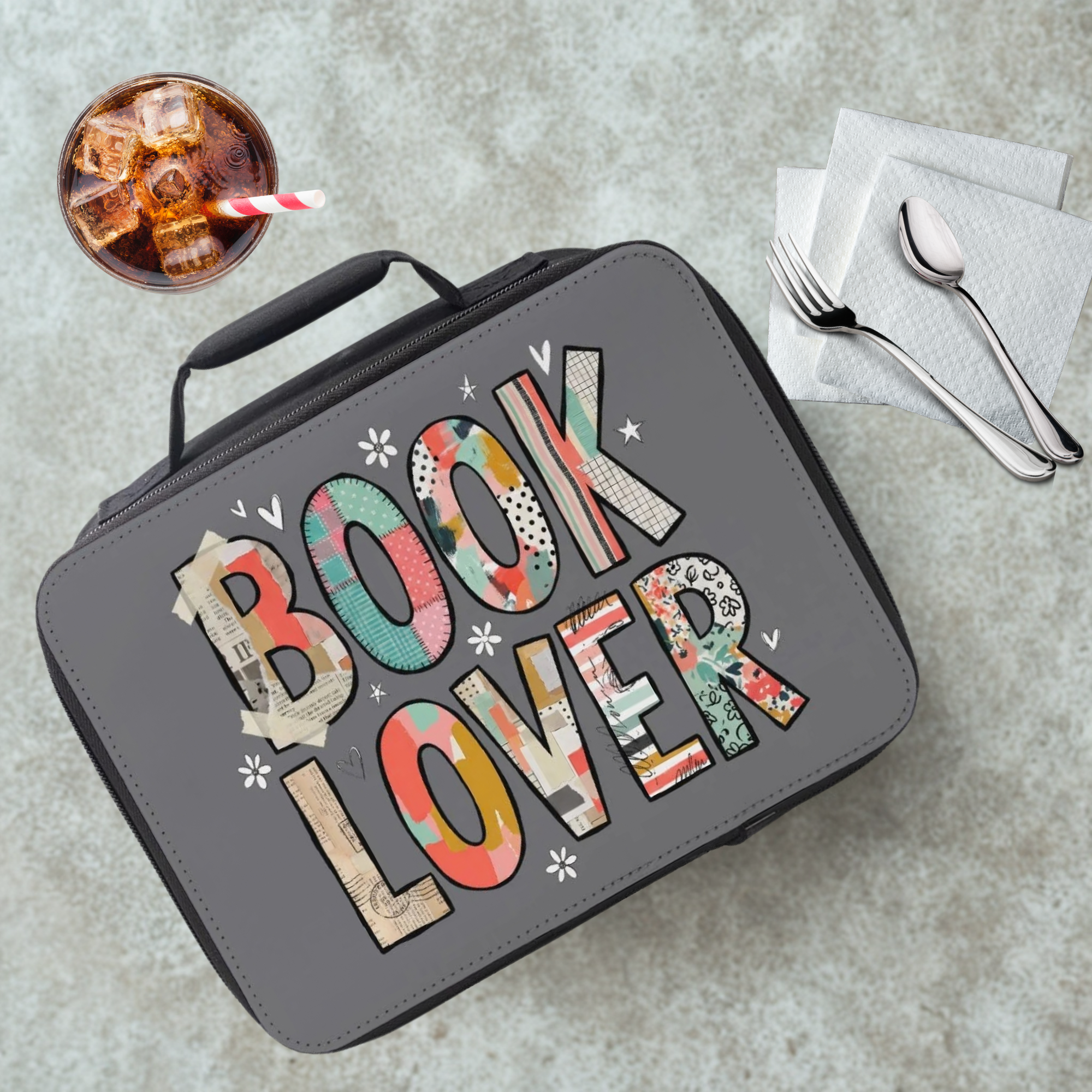 Lunch bag with 'BOOK LOVER' patterned text on a cafeteria table with a drink and utensils.