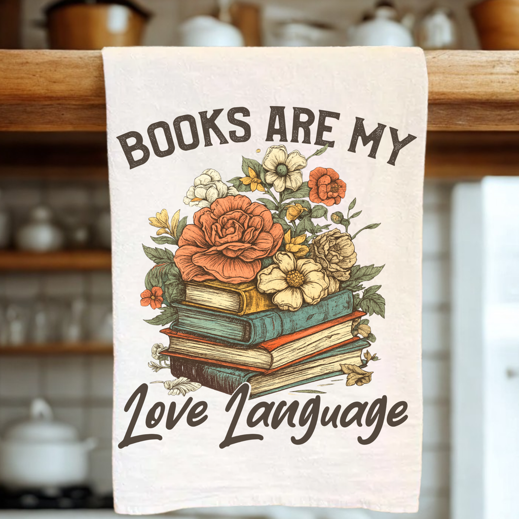 Tea towel with floral design and text 'Books are my love language' hanging on a wooden rack.