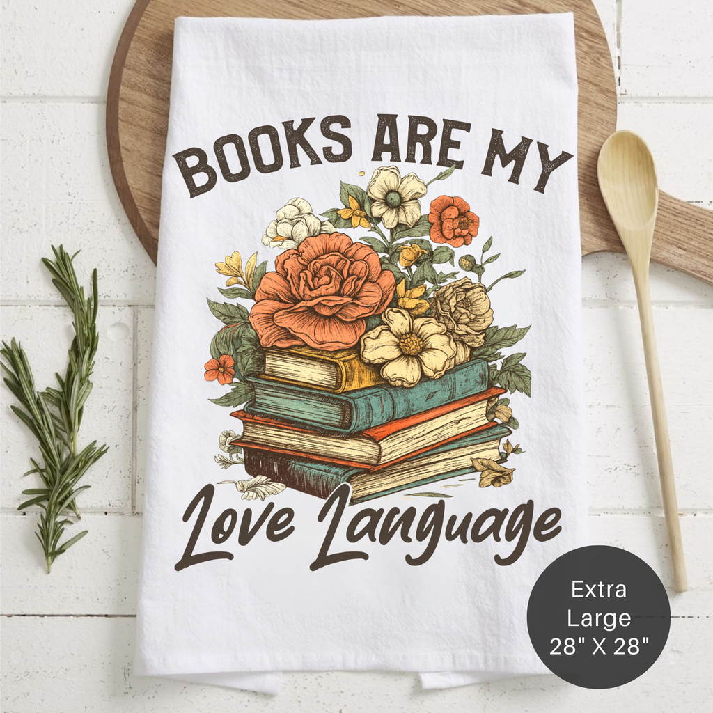 Tea towel with floral design and text 'Books are my love language' on a wooden surface.