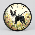 Round wall clock with a black frame and a printed illustration of a black-and-white Boston Terrier standing in a flower field. The clock face has a warm cream background, black Roman numerals, black hour markers, and black hands, shown against a light gray studio background.