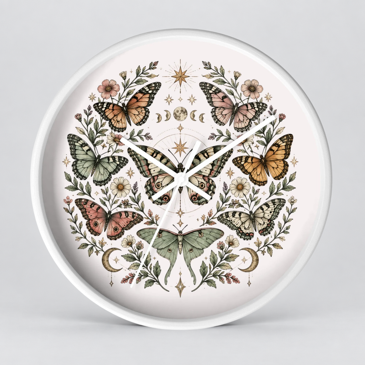 Round wall clock with a white frame and a detailed botanical illustration featuring butterflies, flowers, moons, and stars on a pale pink face, shown against a light gray background.