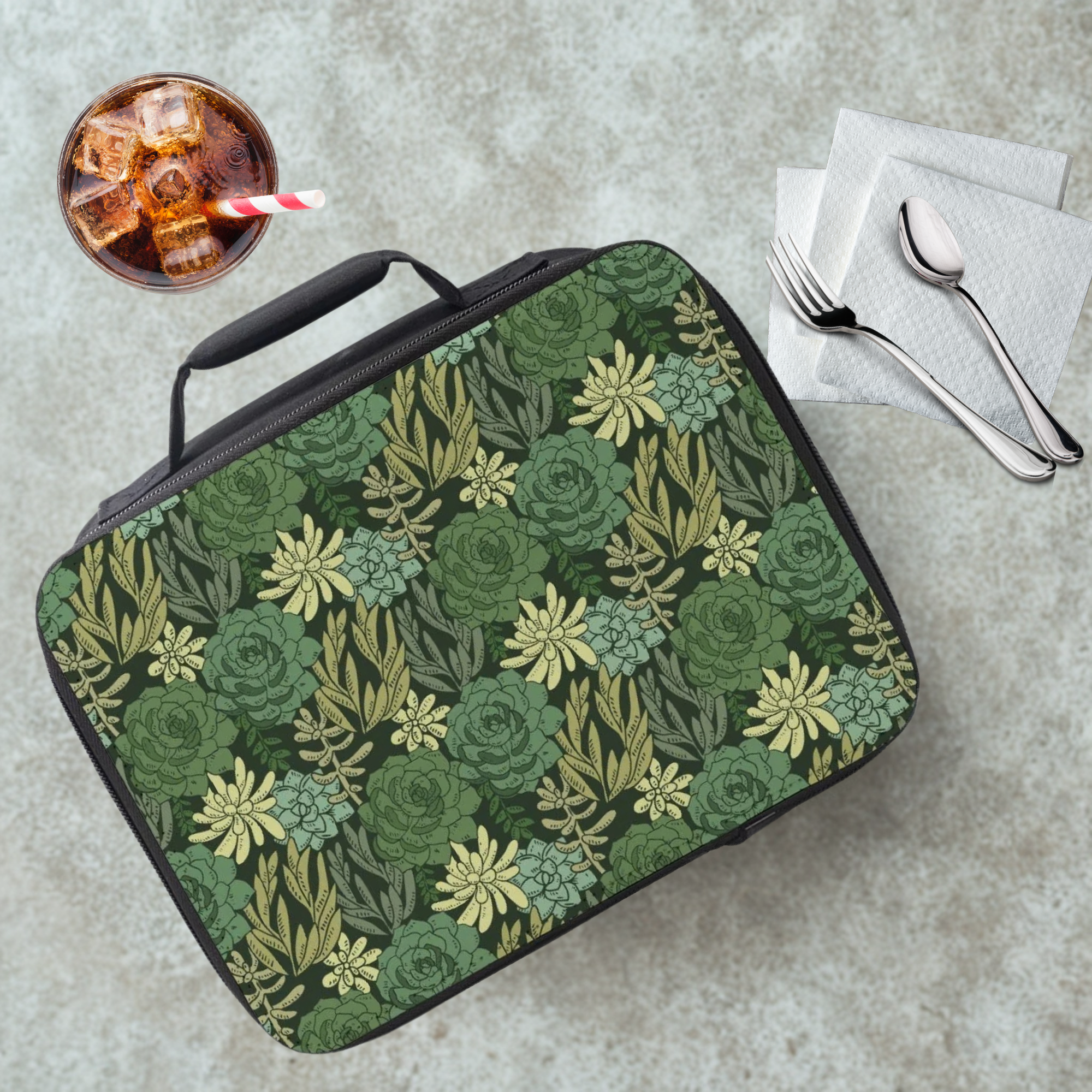 Green floral patterned lunch bag on a table with a drink and utensils.