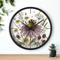 Round black decorative wall clock with a hand drawn bee and flower design on a white background
