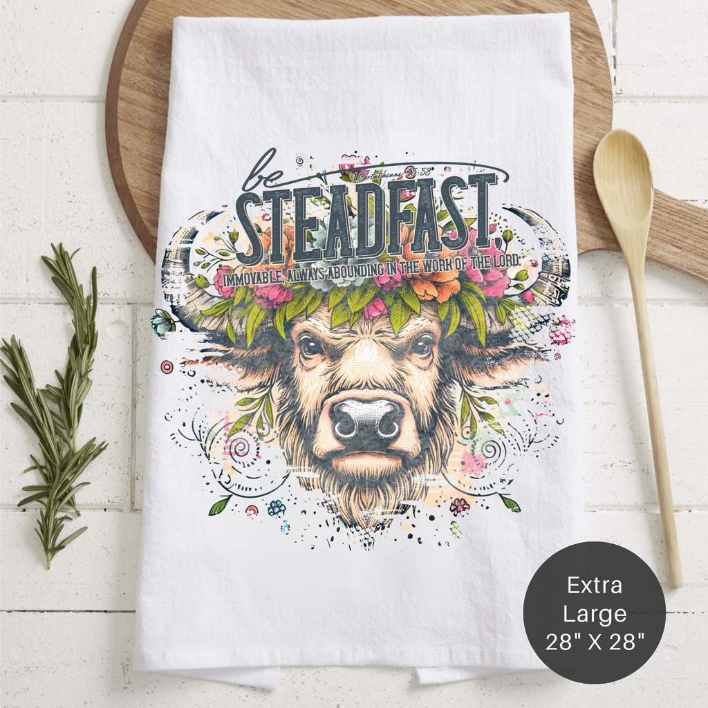 Tea towel with a cow illustration and motivational text on a wooden surface.