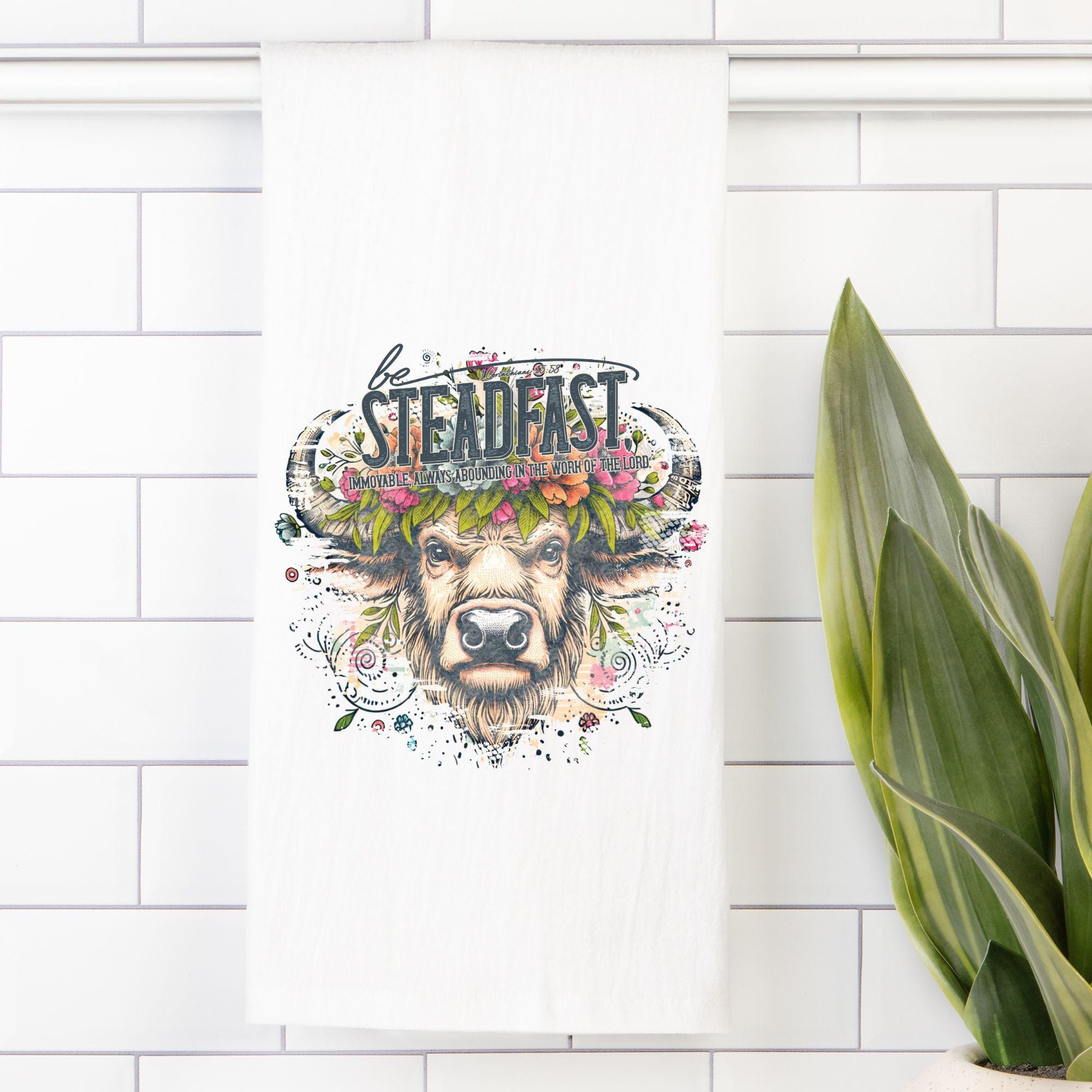 Decorative tea towel with a bull buffalo head and floral crown on a white tiled wall.
