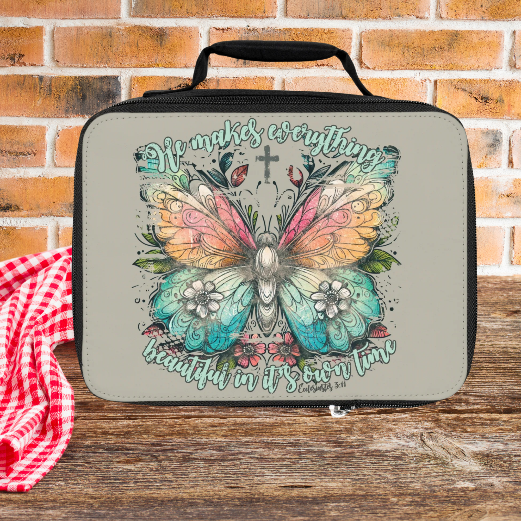 Lunch bag with butterfly design and text on a wooden picnic table against a brick wall background