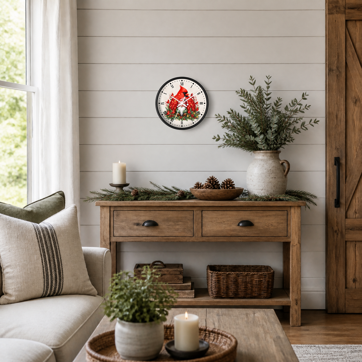 A round wall clock with a black frame and a festive Christmas design featuring red cardinals and green pine branches, styled on a wooden console table in a cozy living room setting.
