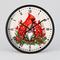 A round wall clock with a black frame and a festive holiday design featuring red cardinals, a gnome in a Santa hat, and green evergreen branches on an off-white textured background with black Roman numerals.