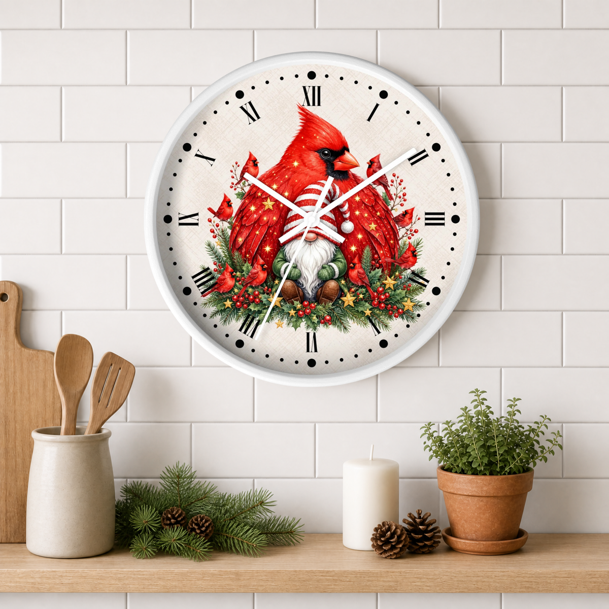 A round wall clock with a white frame and Roman numerals, featuring a festive illustration of two red cardinals, a small gnome, and holiday greenery. The clock is mounted on a white subway tile wall above a wooden shelf styled with kitchen utensils, pine branches, a candle, and a potted plant.