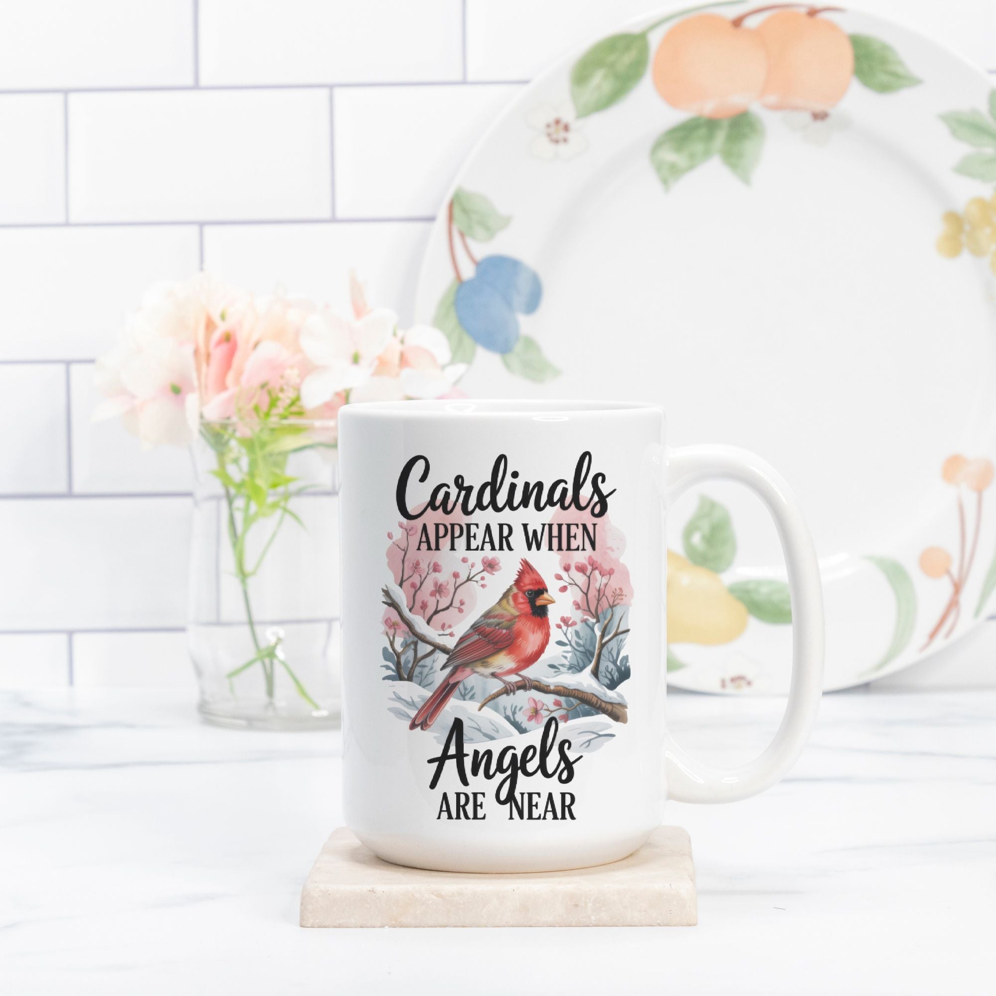 Mug with cardinal design and text on a white surface with a floral plate in the background.