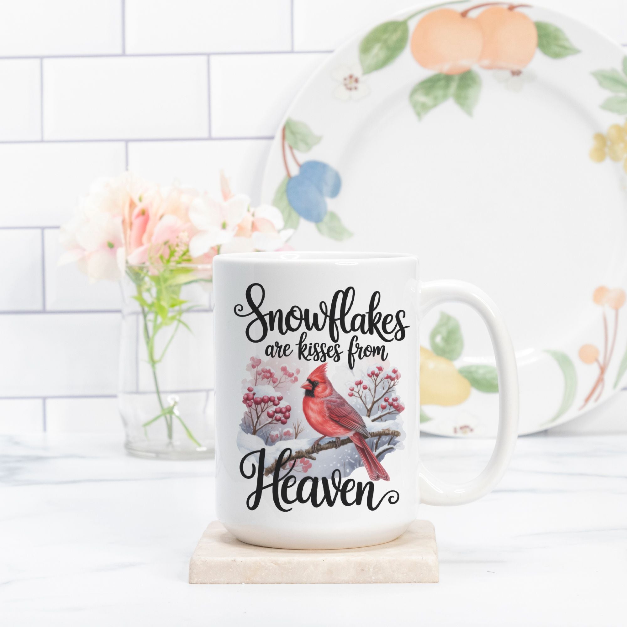 Mug with cardinal design and text on a white surface with a floral arrangement in the background