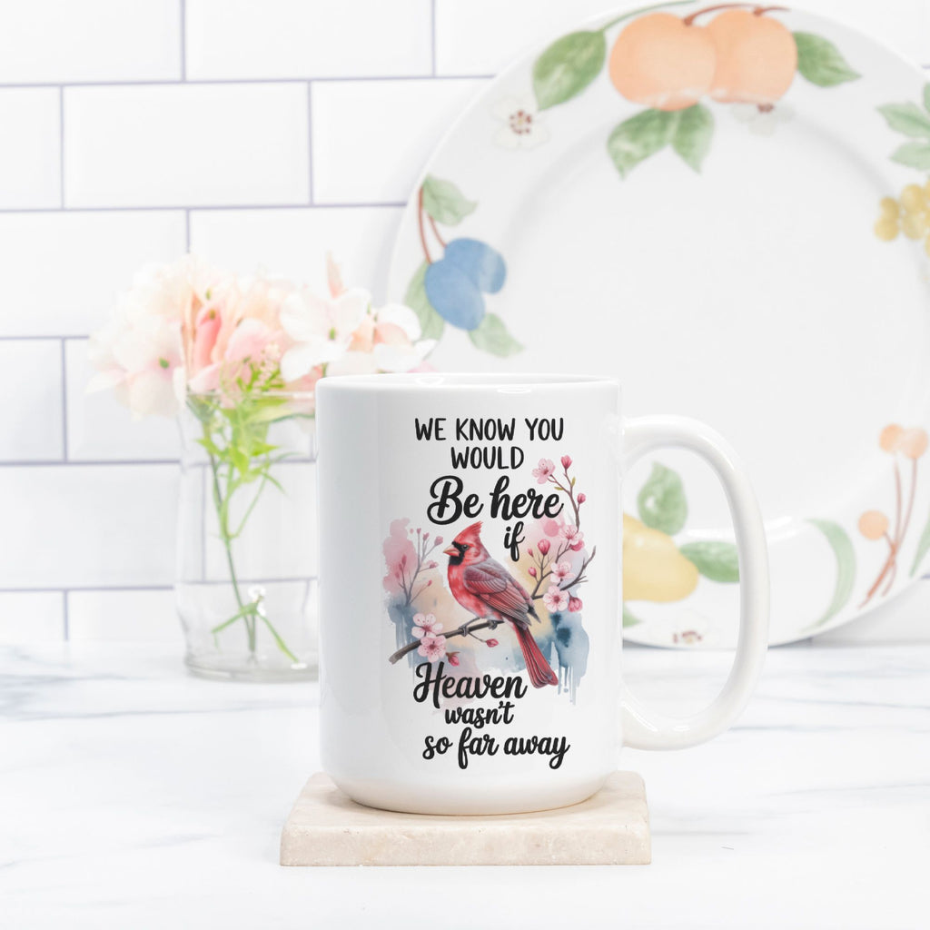Mug with a cardinal design and text on a white surface with a floral plate in the background.