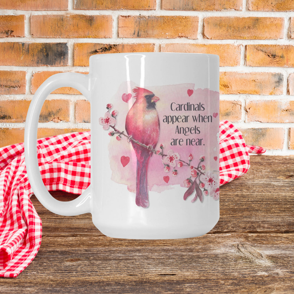 White mug with cardinal design and text on a wooden picnic table with a red and white checkered cloth and brick wall background.