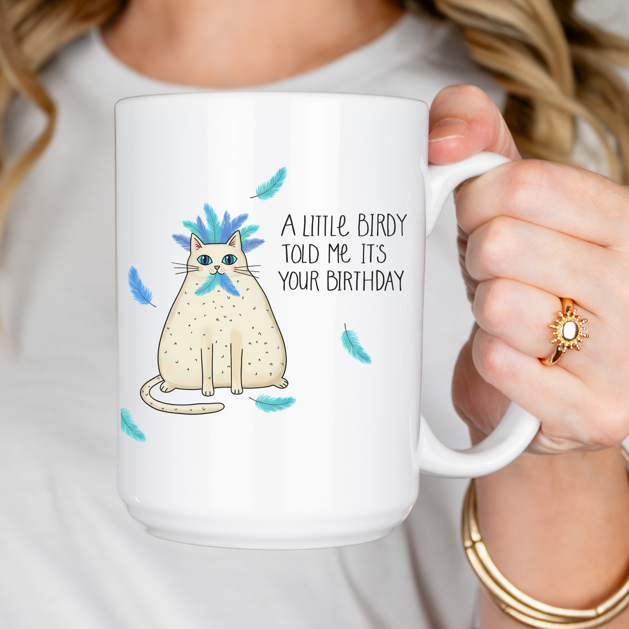 White mug with a cat illustration and birthday message, held by a person.