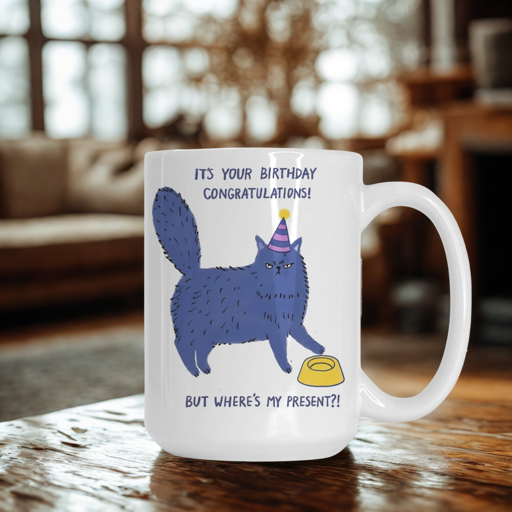 Mug with a blue cat illustration and birthday text on a wooden table.