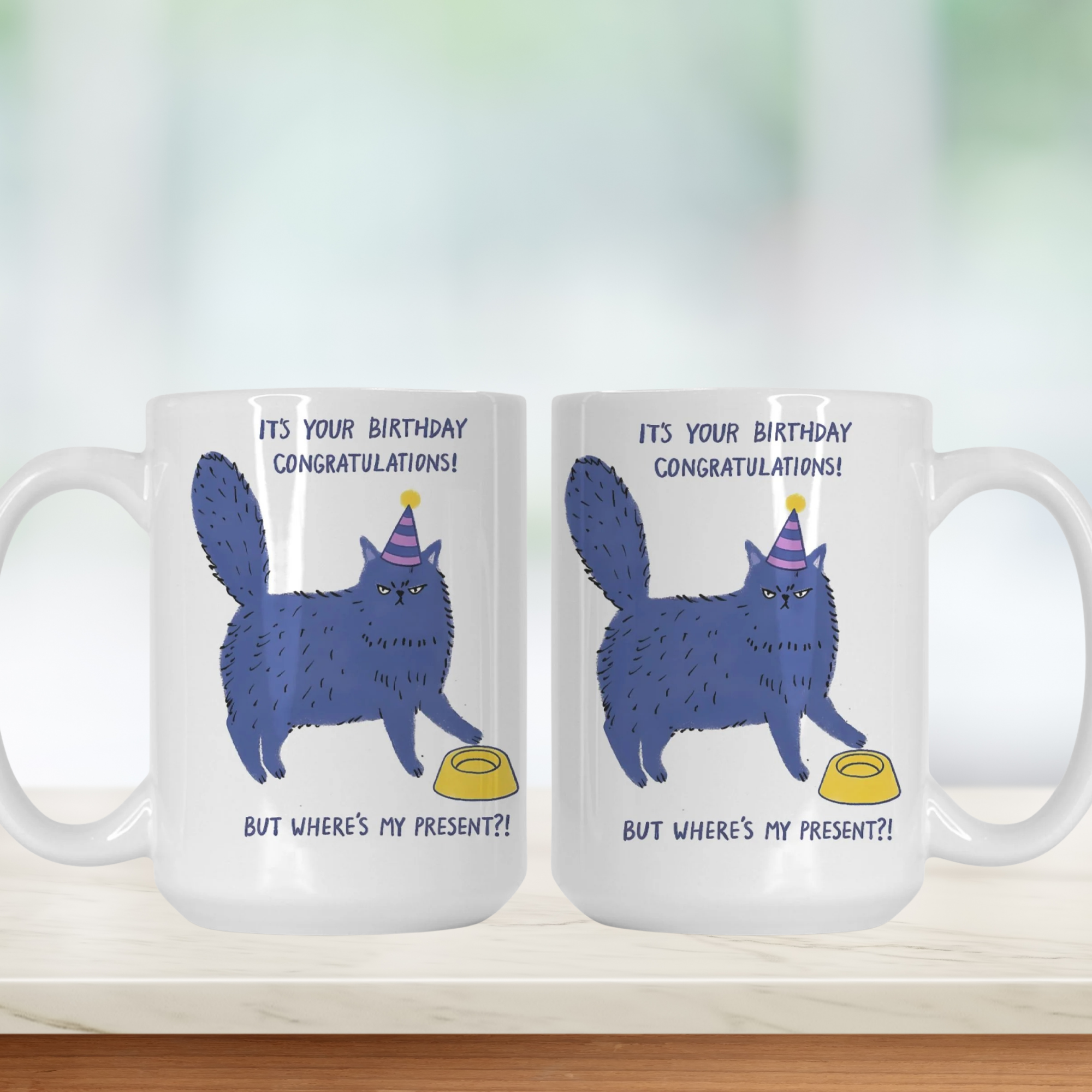 Two white mugs with a blue cat illustration and birthday text on a white background