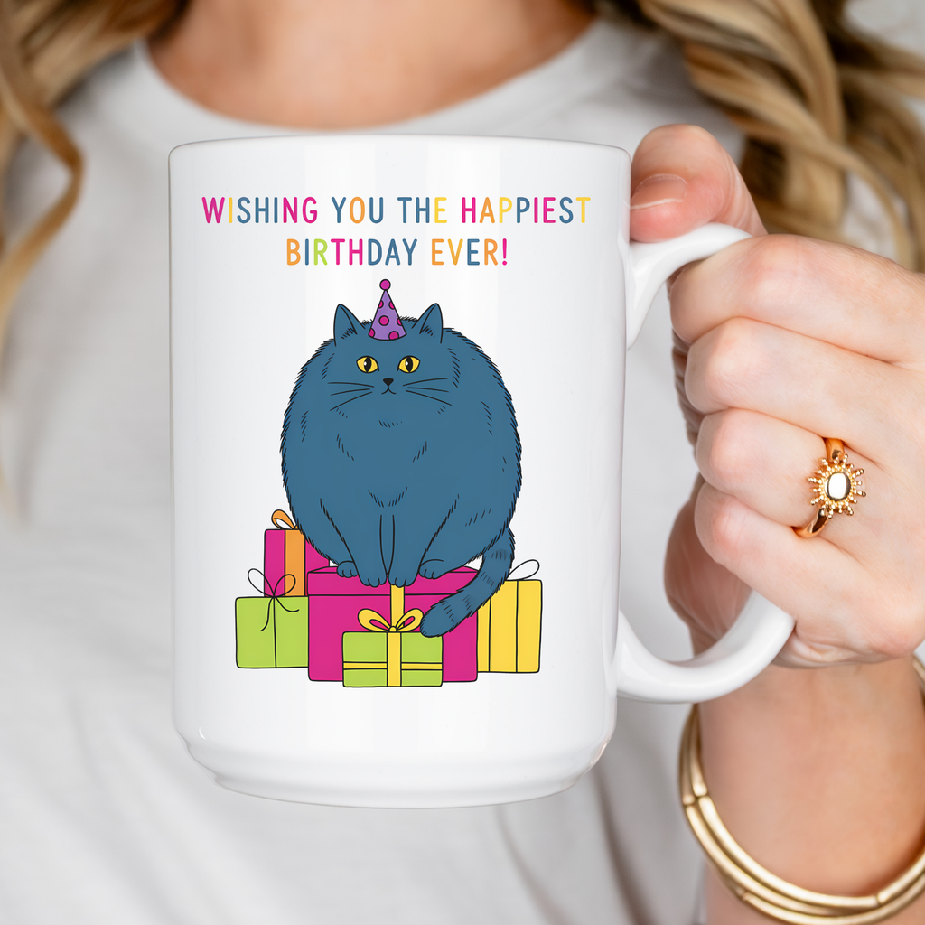 Mug with a blue cat on presents and 'Happiest Birthday Ever' text, held by a person.