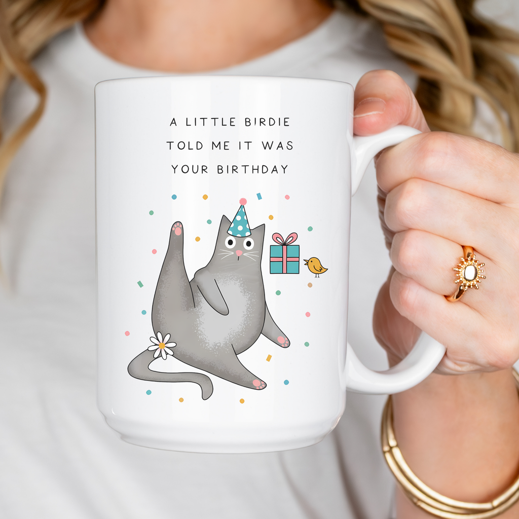 Person holding a mug with a cat illustration and birthday text