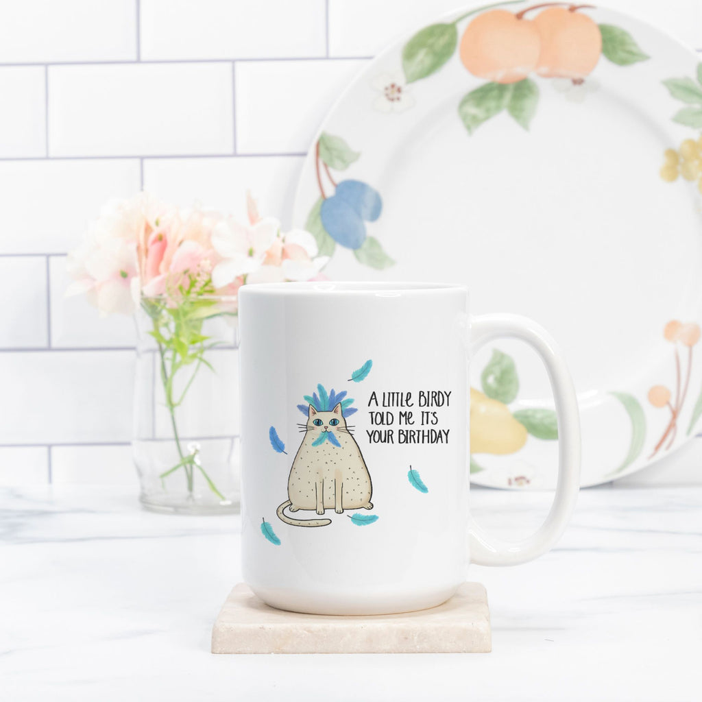 White mug with a cat illustration and text, placed on a white surface with a floral plate in the background.