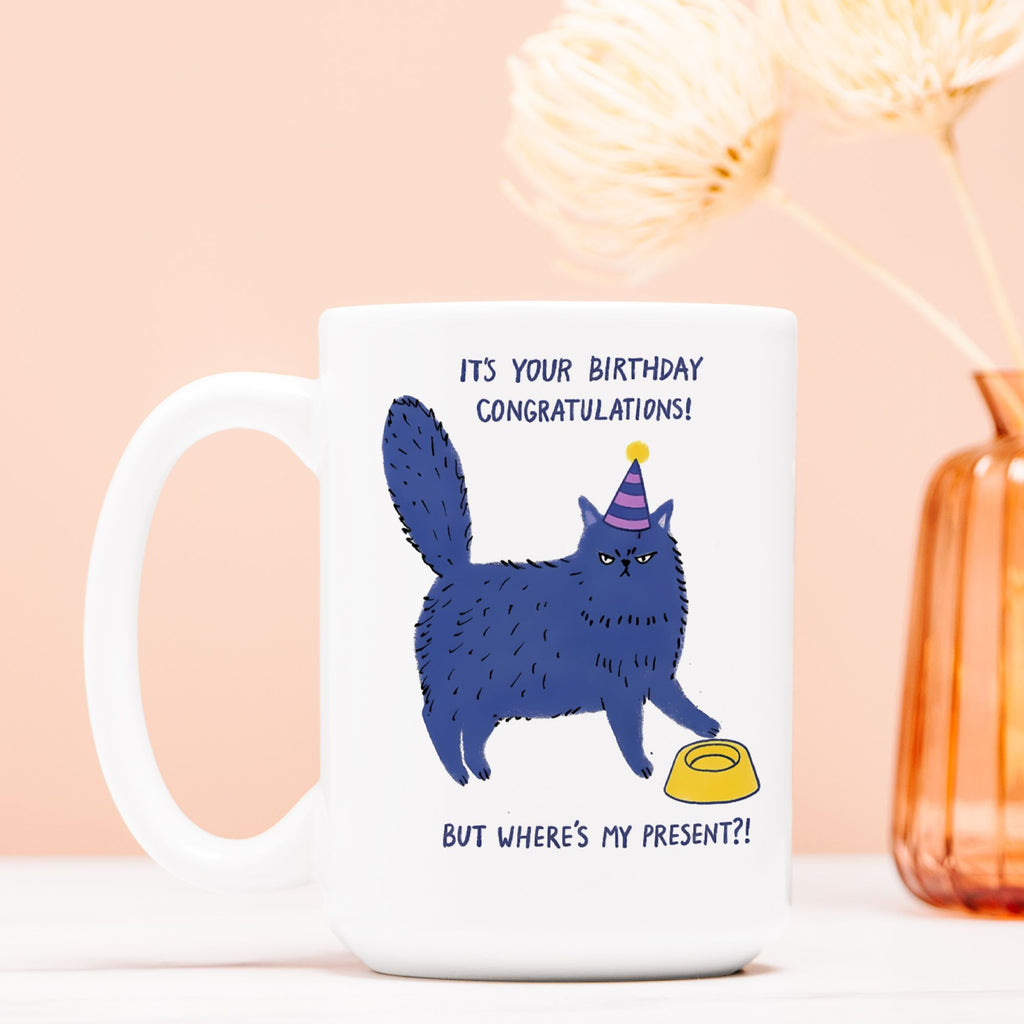 White mug with a blue cat illustration and text on a peach background