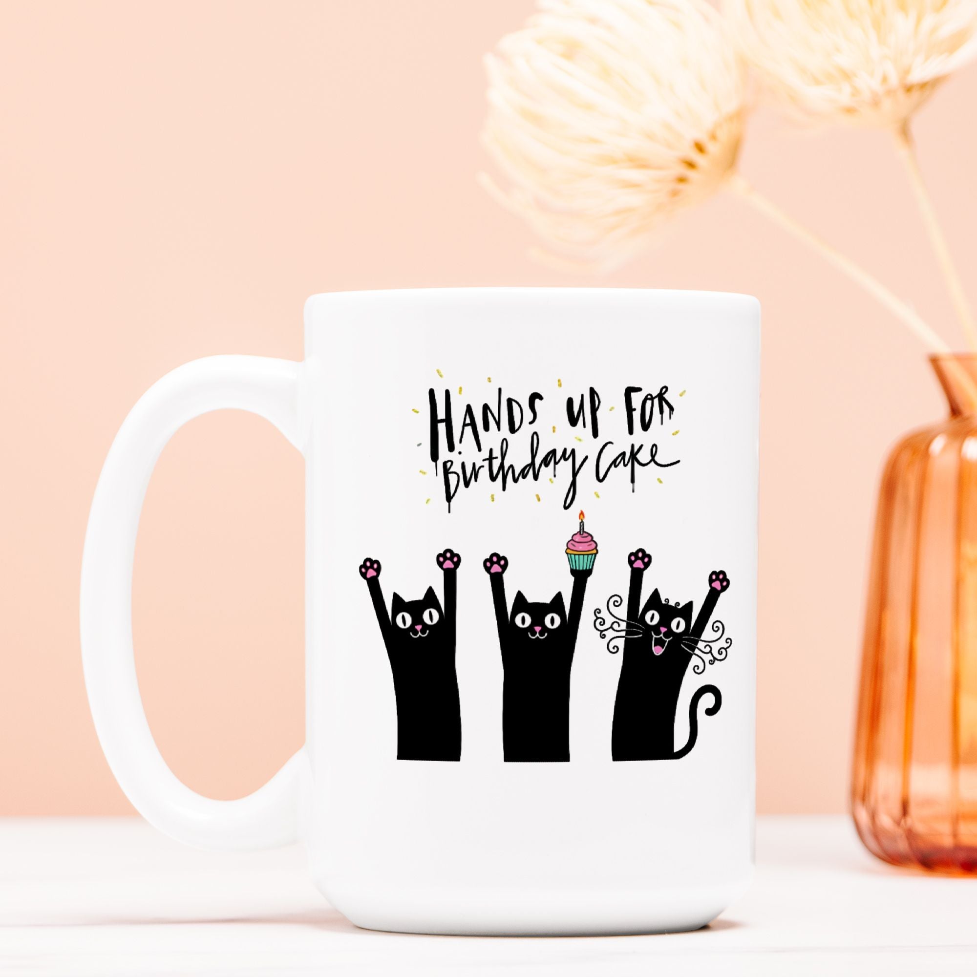 White mug with black cat illustrations and birthday text on a light pink background