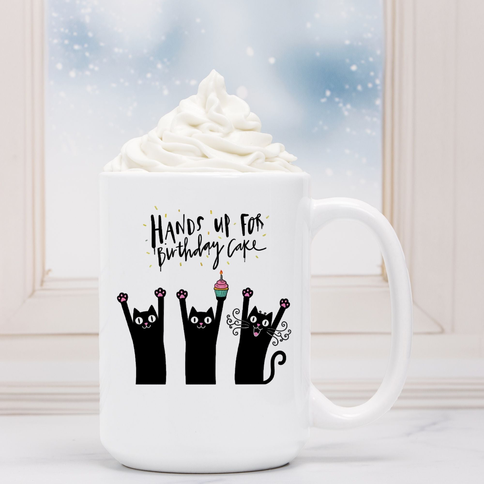 White mug with black text and cat illustrations, placed on a surface with a blurred background.