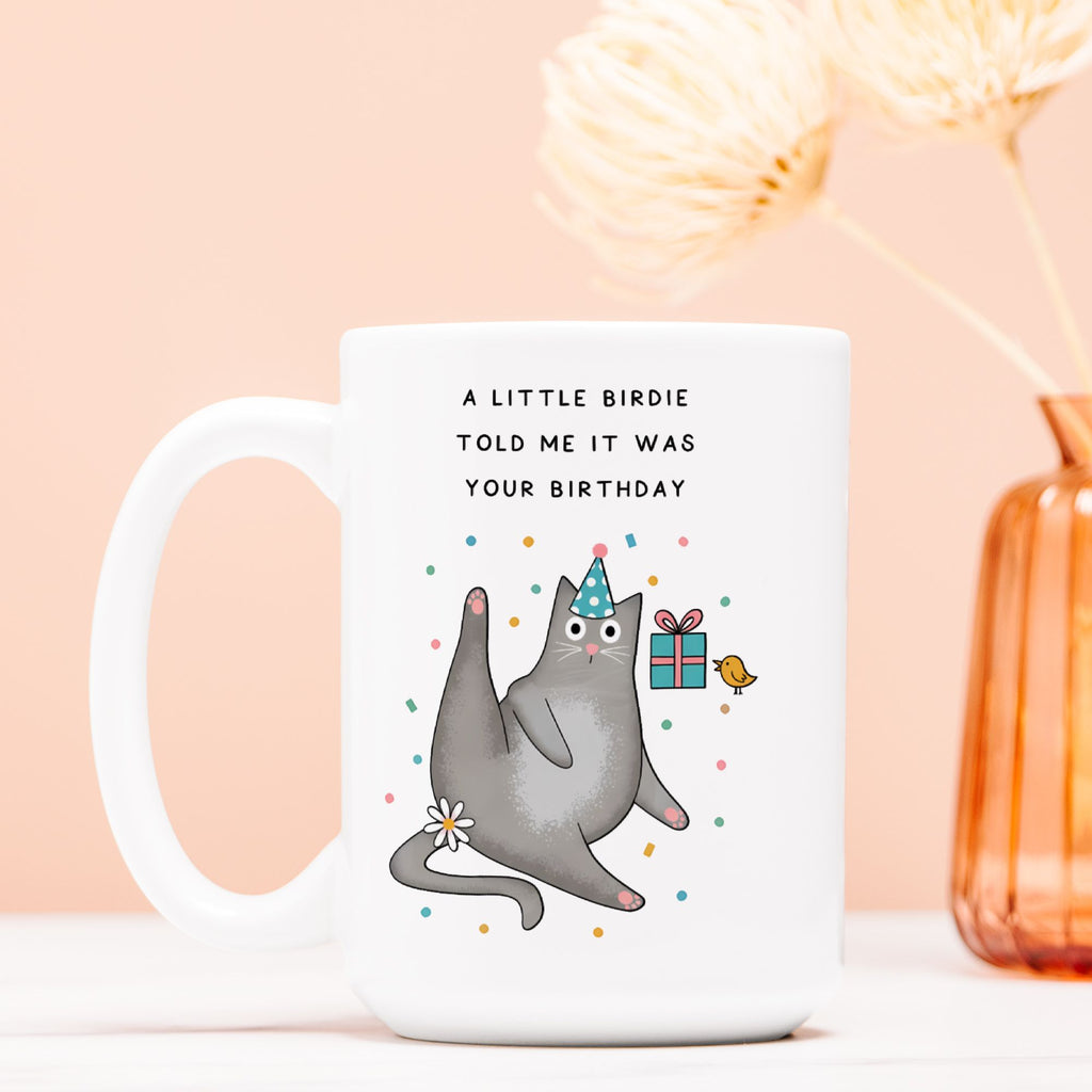 White mug with a cat illustration and birthday text on a light pink background