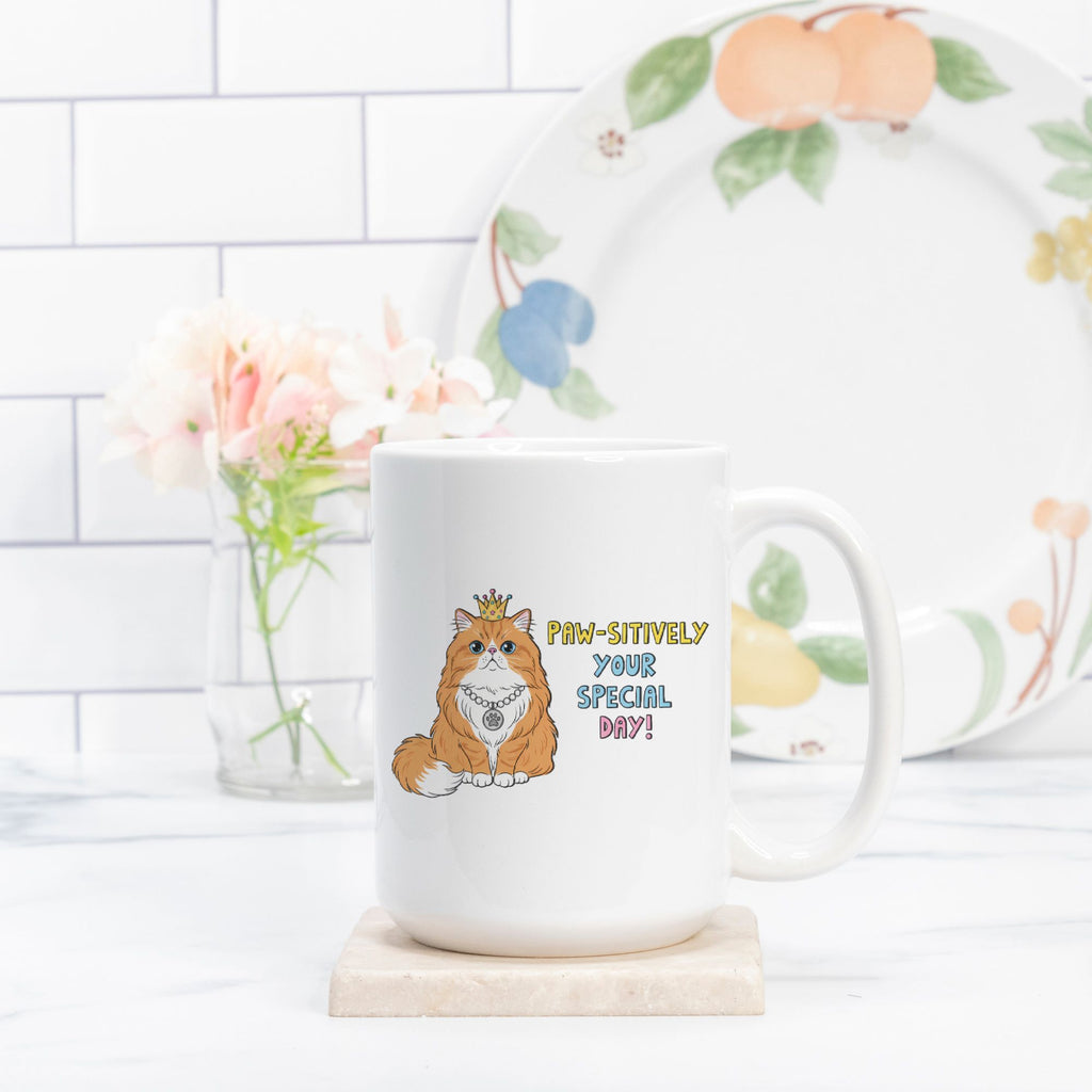 White mug with a cat design and 'Paw-Sitively Your Special Day!' text on a white surface with a floral plate in the background.
