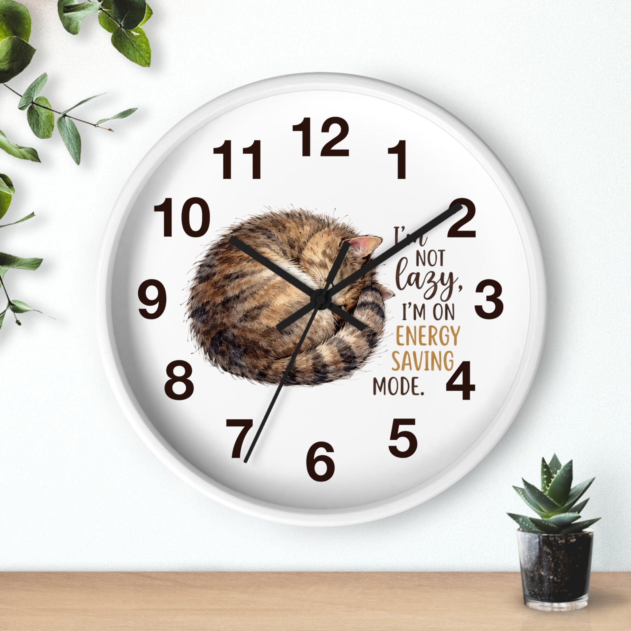 Round white wall clock with a cat design and humorous text on a white background
