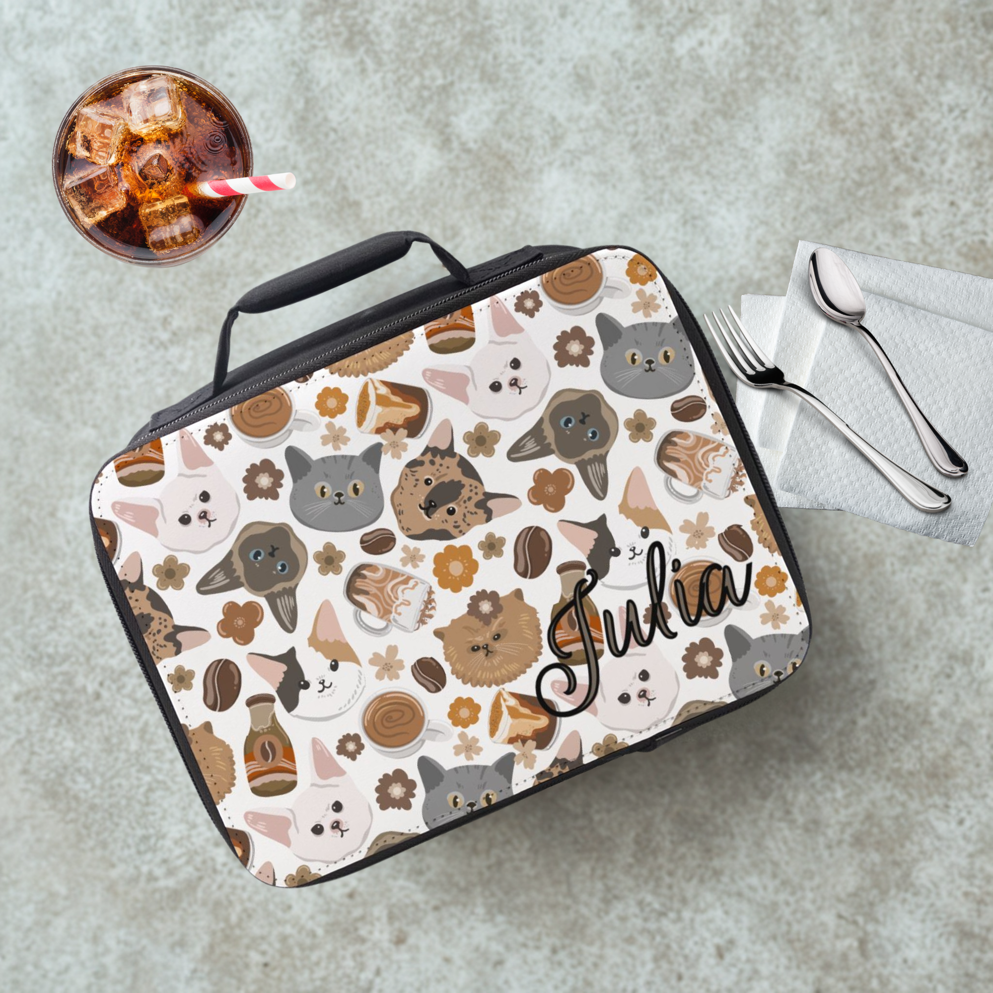 Lunch bag with cat pattern and 'Julia' branding on a cafeteria table with a drink and utensils.