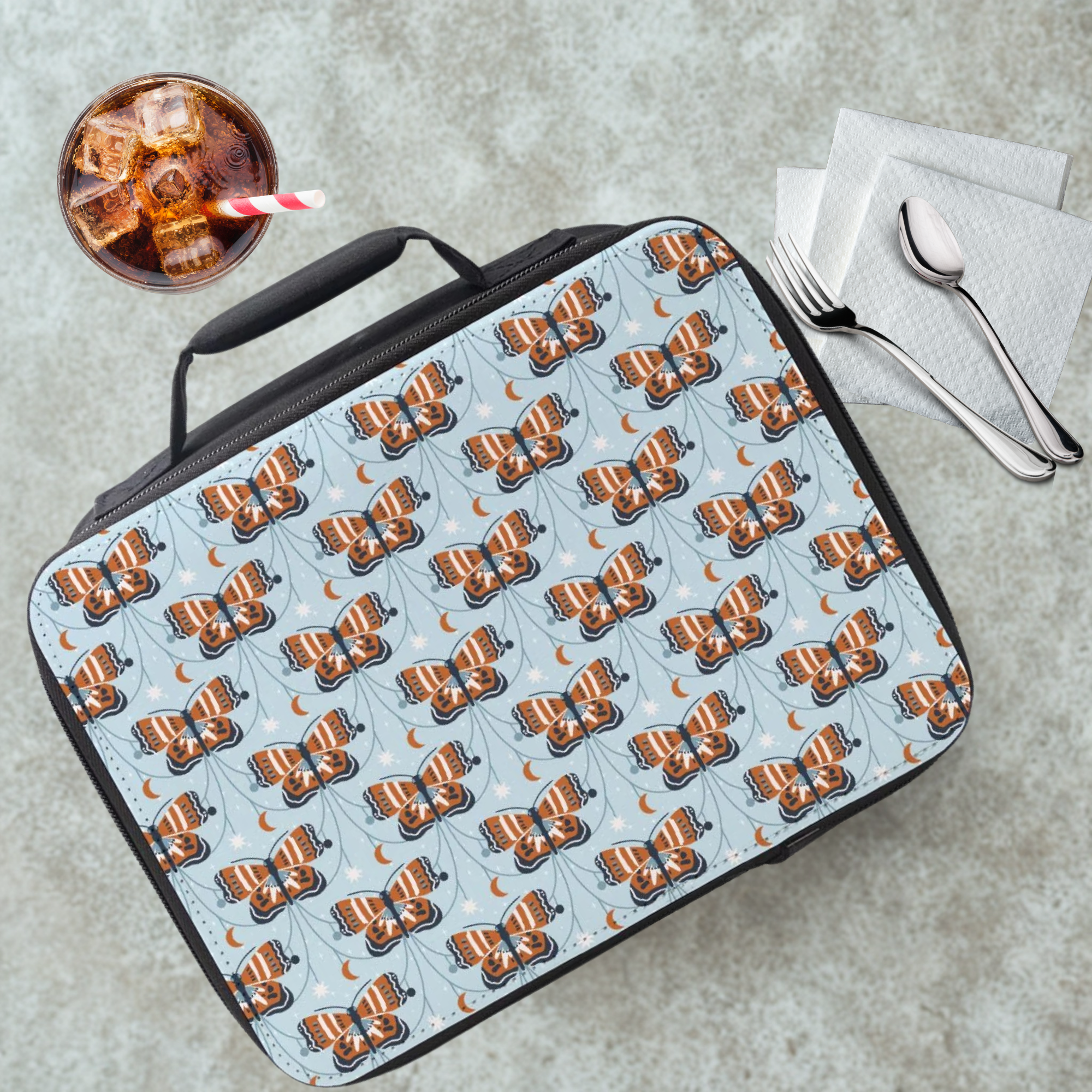 Lunch bag with butterfly pattern on a cafeteria table with a drink and utensils.