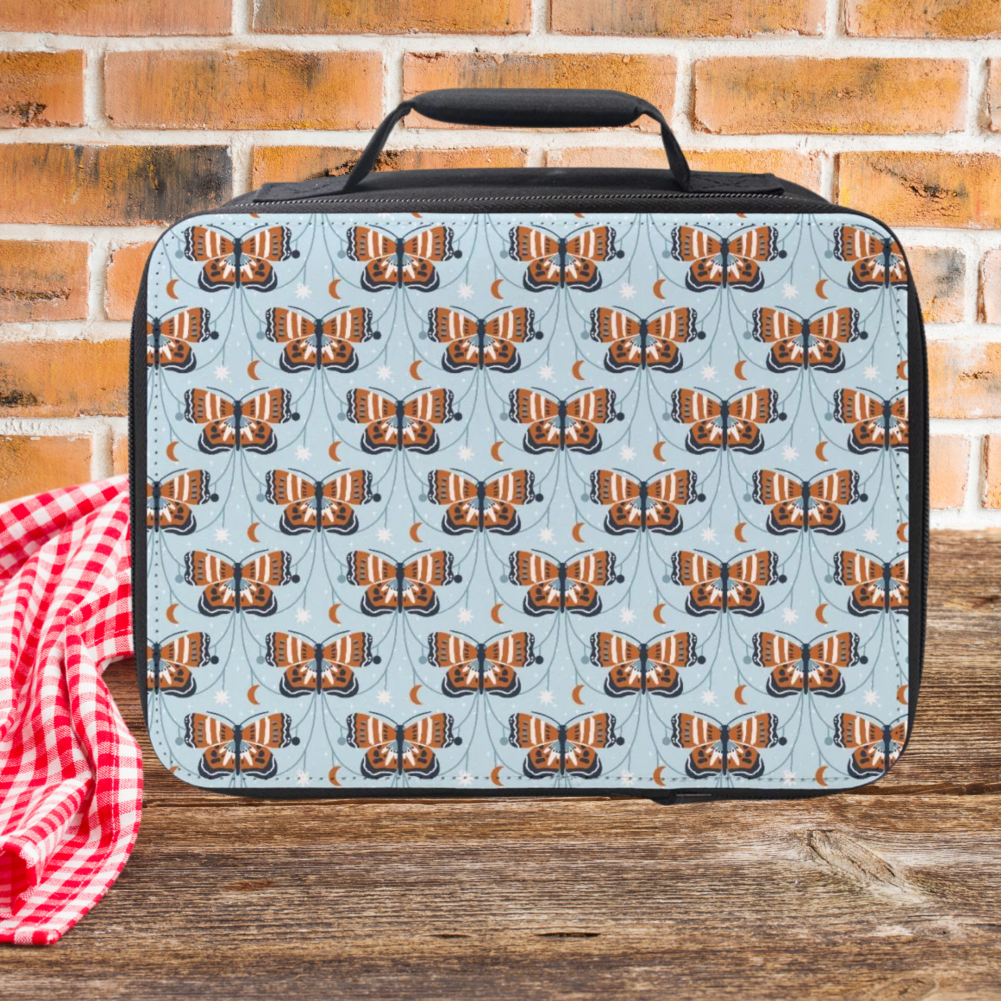 Lunch bag with butterfly pattern on a wooden picnic table against a brick wall background