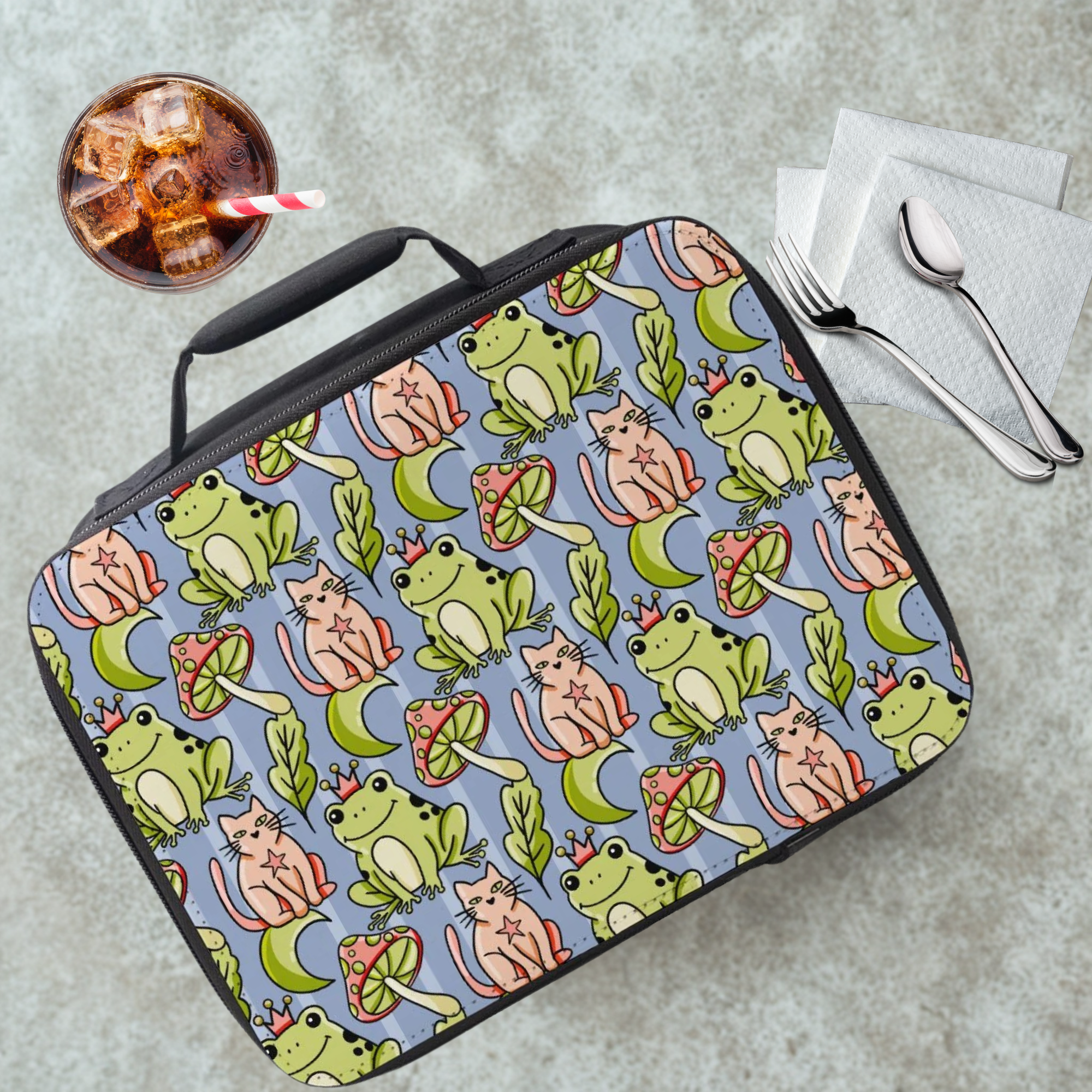 Lunch bag with frog and cat pattern on a cafeteria table with a drink and utensils.
