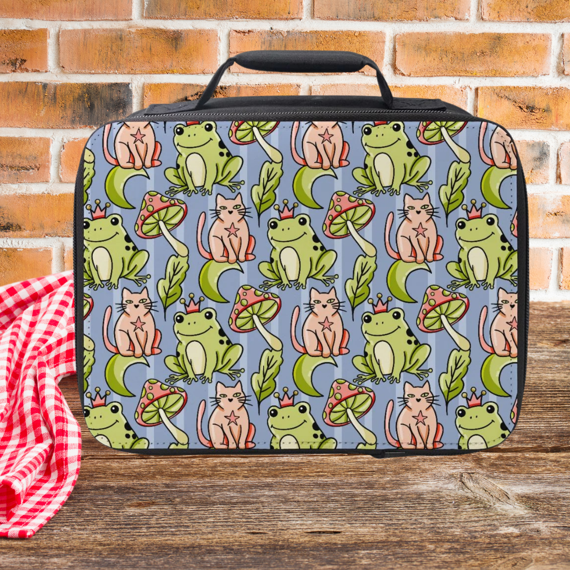 Lunch bag with frog and cat pattern on a wooden picnic table and brick wall background